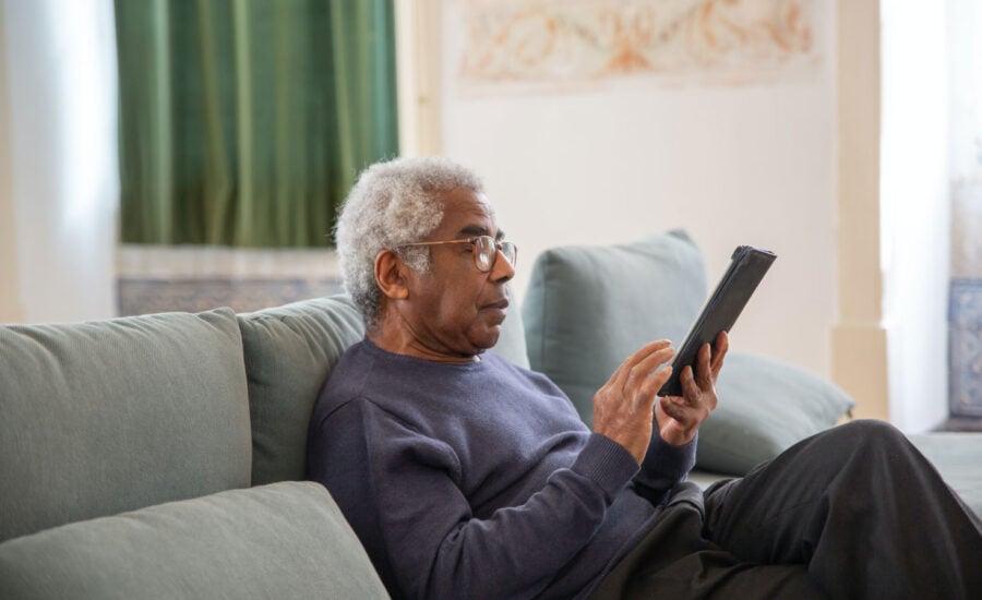 A man, sitting at home on his couch, is scrolling through his iPad calendar, to choose a date to retire.