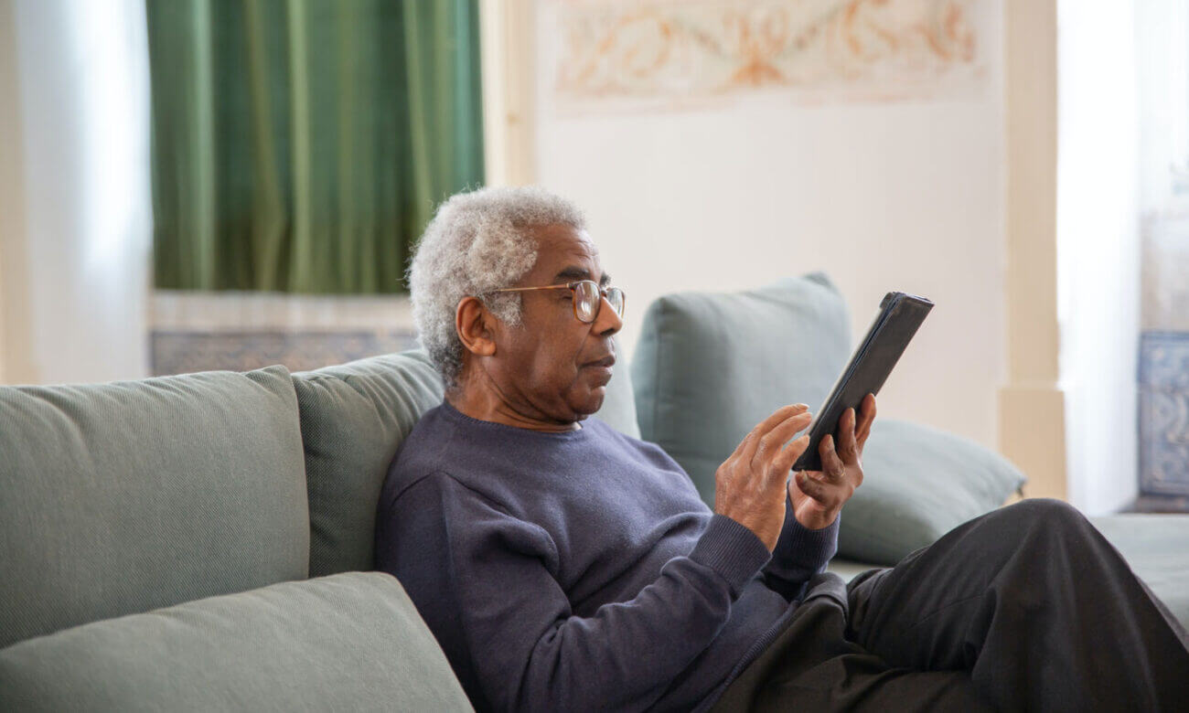 A man, sitting at home on his couch, is scrolling through his iPad calendar, to choose a date to retire.