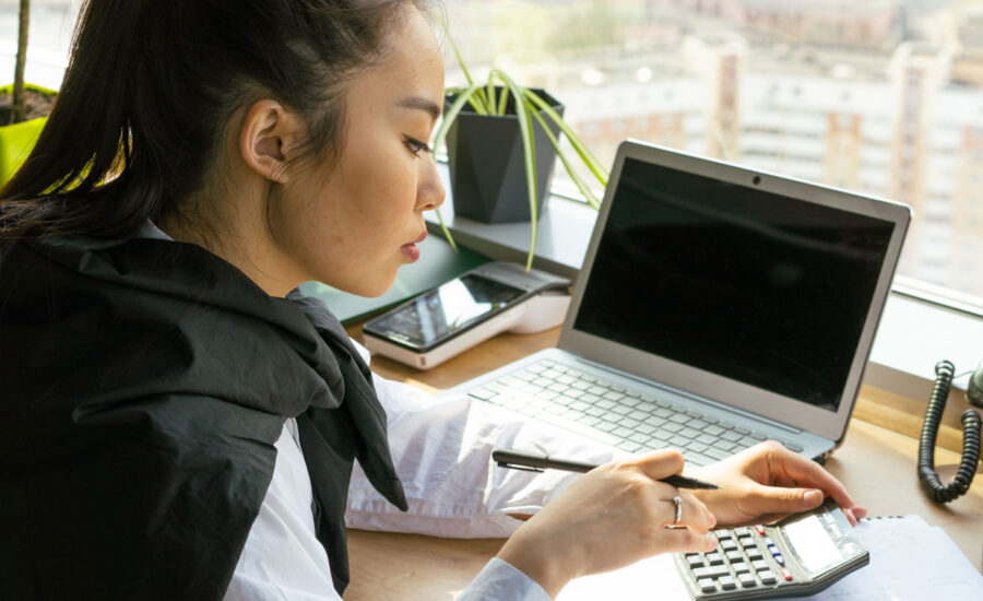 A woman is sitting at her desk, using her calculator to figure out her debt-to-income ratio.