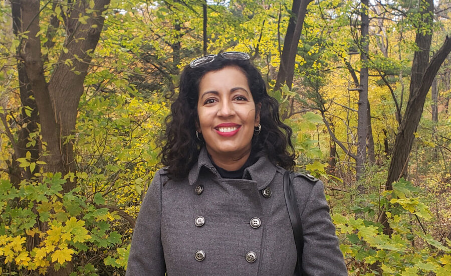 Renée Sylvestre-Williams smiles in a headshot of her taken on a beautiful fall day near some trees.