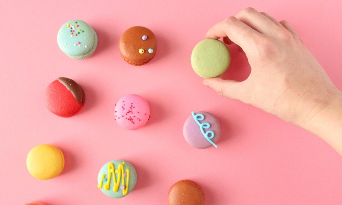 A hand picking up a macaron from a colourful assortment