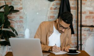 A man sits at a café table writing notes