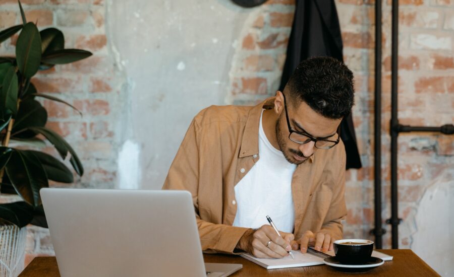 A man sits at a café table writing notes