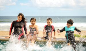 A young woman and three kids splash their feet in a beachside pool