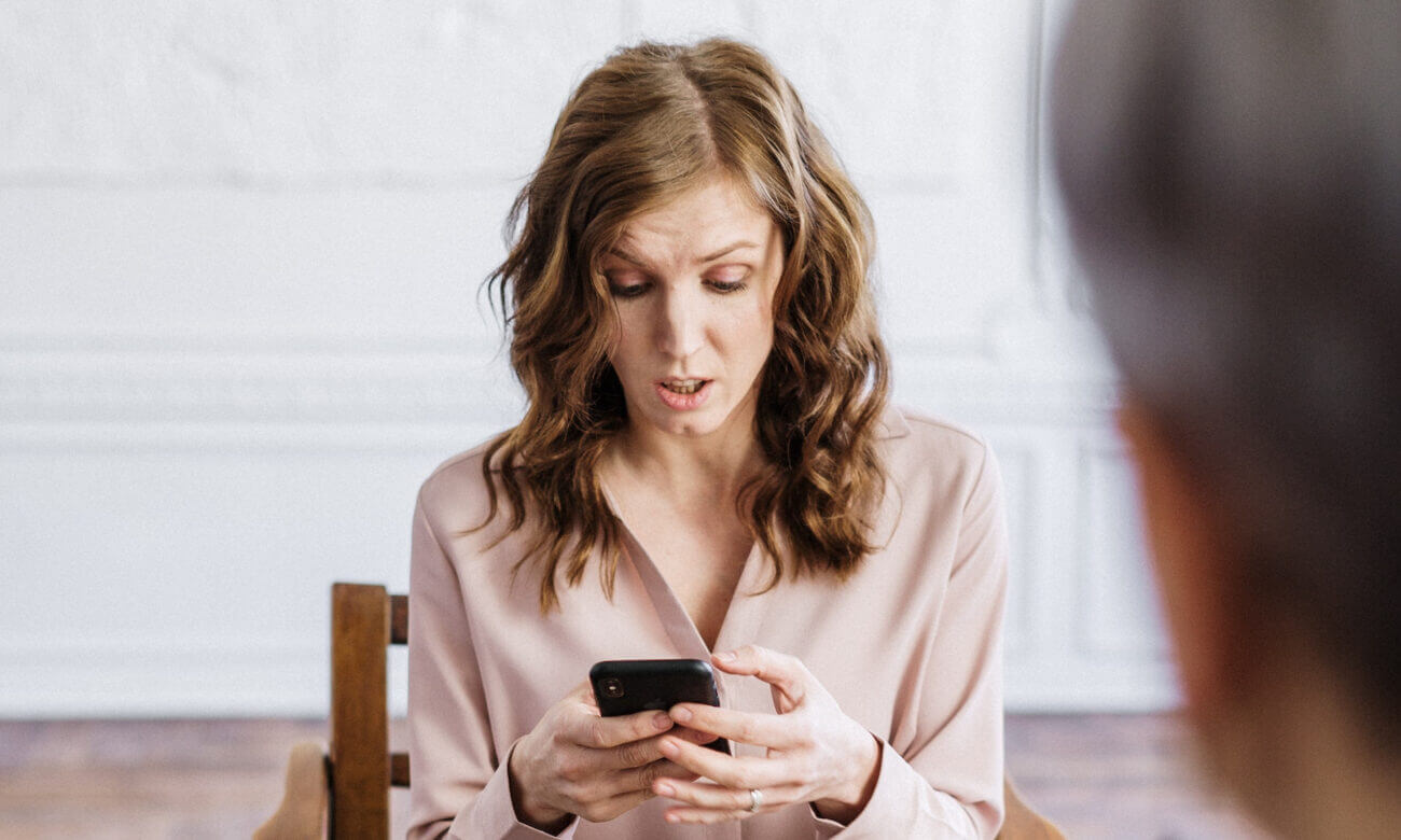 A woman stares at her cell phone in disbelief after learning that she has overcontributed to her TFSA