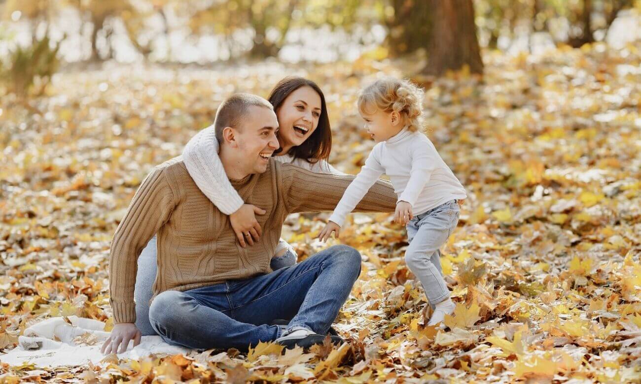 A father, mother and their toddler daughter play in the autumn leaves
