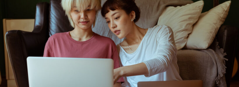 Two women sit on the floor with laptops researching HISA rates