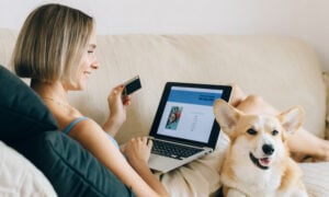 A woman sits on a couch with her dog shopping online with her low-interest credit card