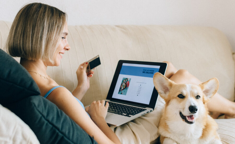 A woman sits on a couch with her dog shopping online with her low-interest credit card