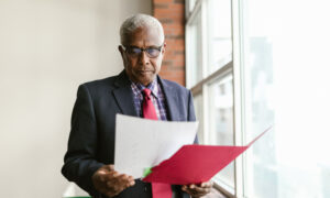 A man reviews paperwork from his corporation while standing near his office window