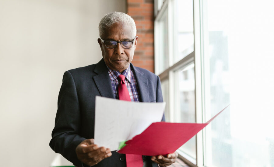 A man reviews paperwork from his corporation while standing near his office window