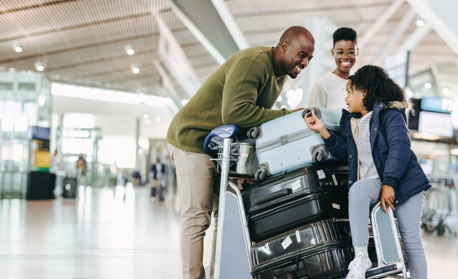 A smiling man, woman and young girl with a stack of suitcases at an airpoty