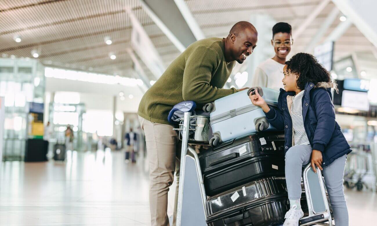 A smiling man, woman and young girl with a stack of suitcases at an airpoty