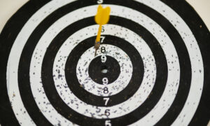 A black and white dartboard struck with a yellow dart illustrates the importance of setting financial goals