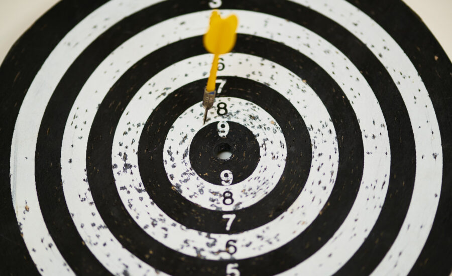 A black and white dartboard struck with a yellow dart illustrates the importance of setting financial goals
