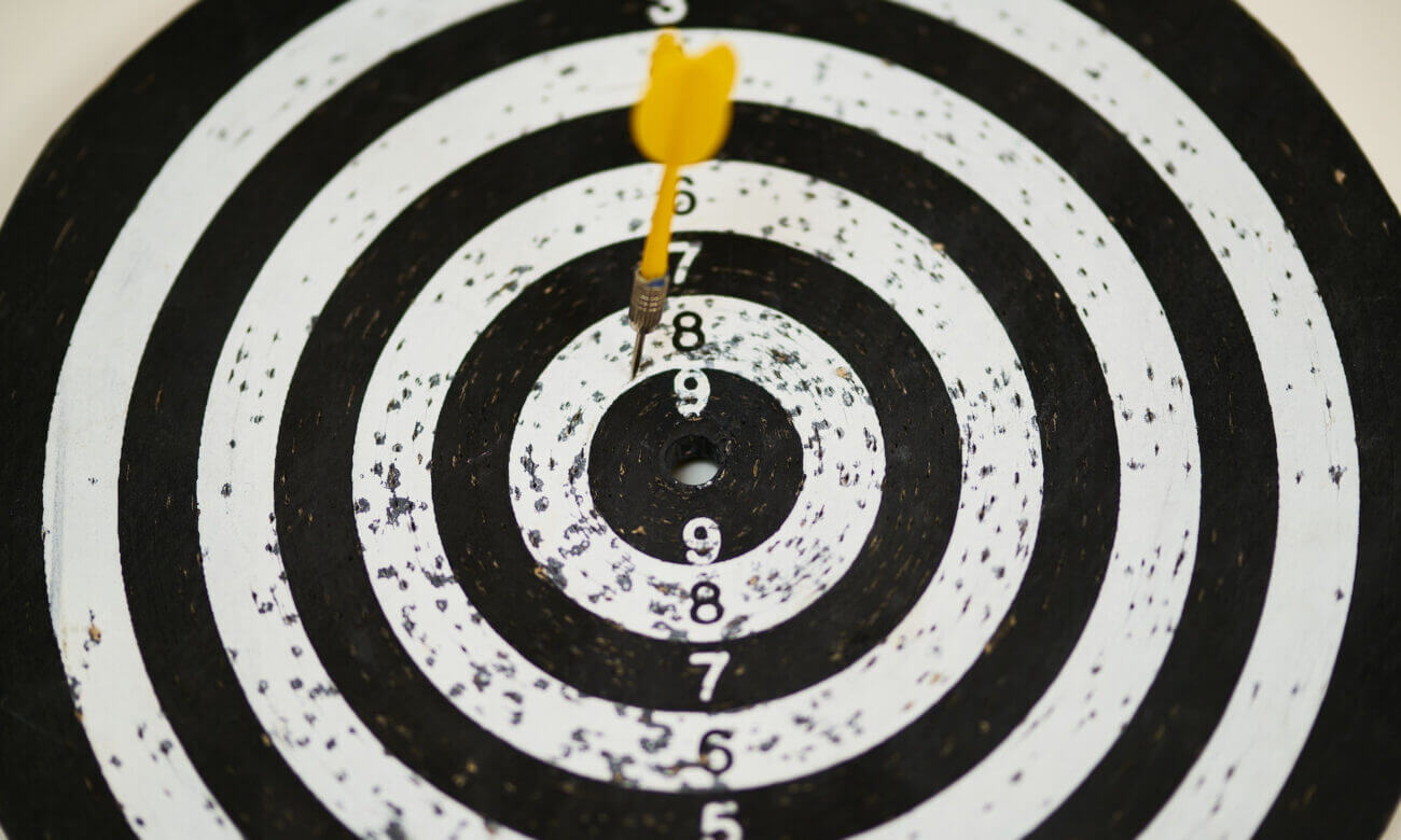 A black and white dartboard struck with a yellow dart illustrates the importance of setting financial goals