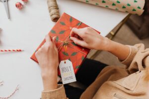 Hands tie a bow on a box wrapped in Christmas paper