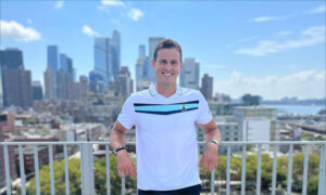 Tennis player Vasek Pospisil leans on a balcony while smiling for the camera on a sunny day.