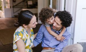 A young woman, man and toddler sit on the doorstep of a house