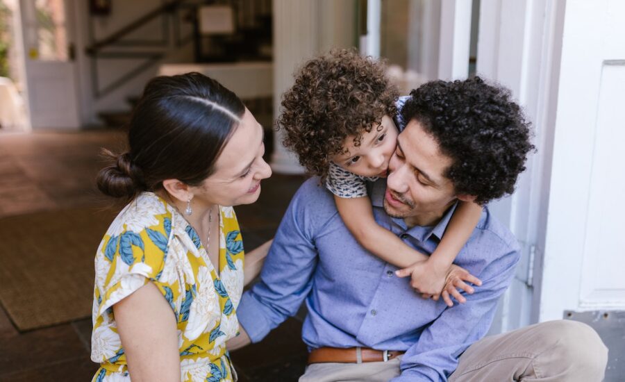 A young woman, man and toddler sit on the doorstep of a house