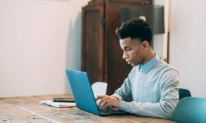 A young man enters the details of his budget on a laptop