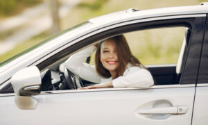 A young woman is driving with the roof down of her convertible, enjoying the low insurance rate she got from taking driving courses.