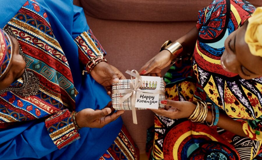 A woman gives a wrapped Kwanzaa gift to another woman