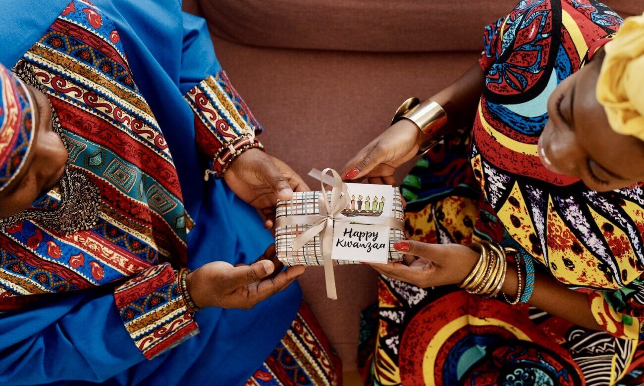 A woman gives a wrapped Kwanzaa gift to another woman