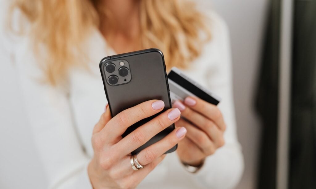 A woman holds her smartphone and a credit card