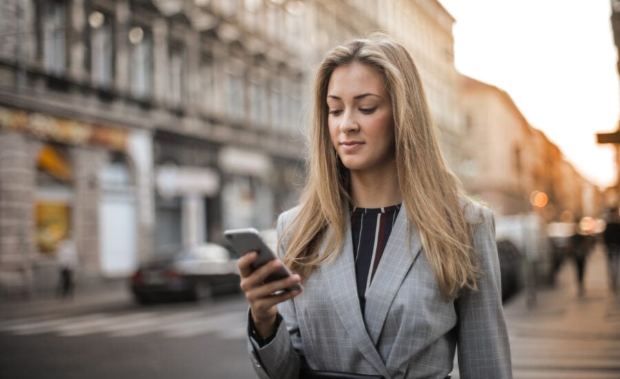 On the street, a well-dressed woman reviews for finances using an app on her phone