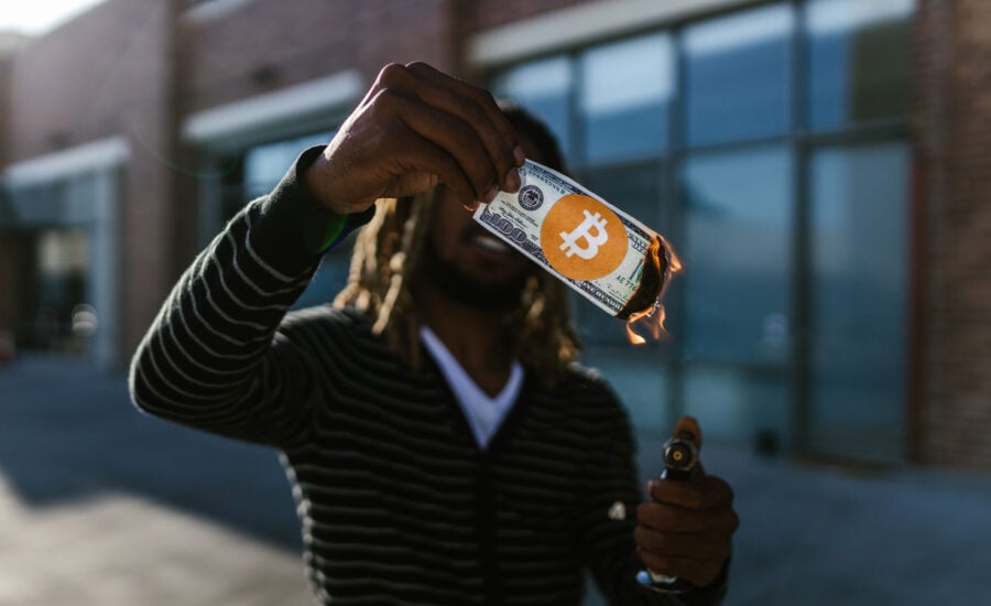 A man holds a dollar bill with a bitcoin sticker, symbolizing the recent fall of FTX and cryptos big falls