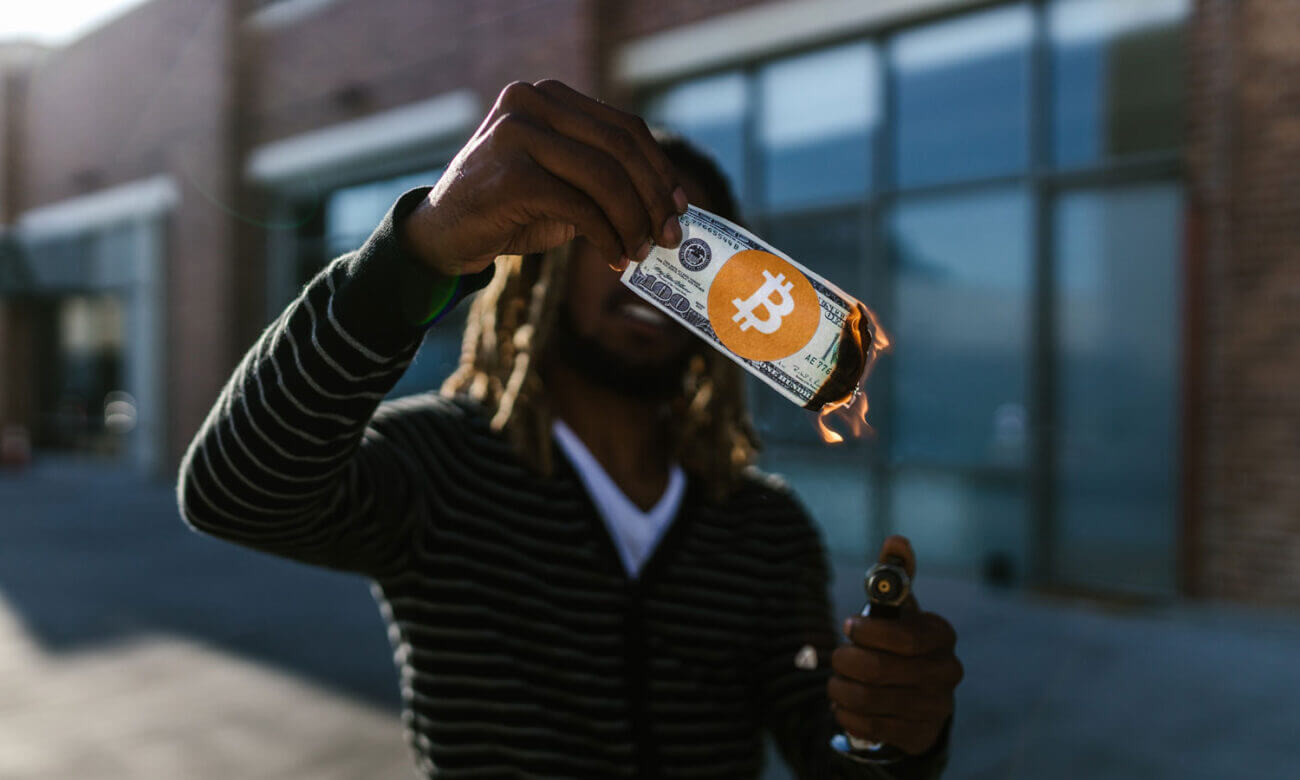 A man holds a dollar bill with a bitcoin sticker, symbolizing the recent fall of FTX and cryptos big falls