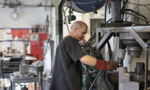 A man in his 60s adjusts a part on a greasy machine at work