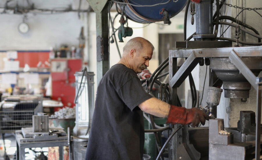 A man in his 60s adjusts a part on a greasy machine at work