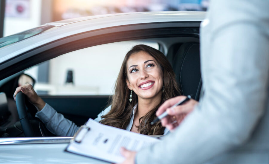 A woman sits behind the wheel of a car, smiling at a salesperson