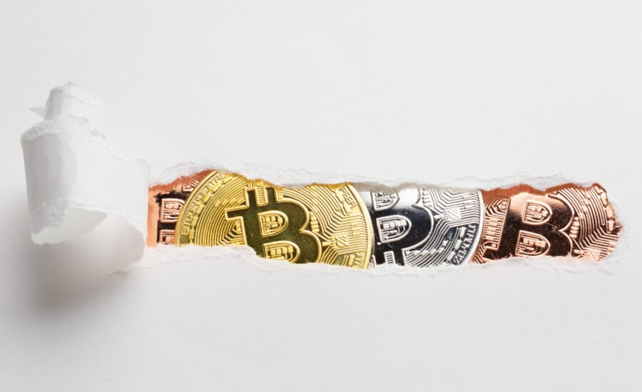 A strip of paper torn open to reveal three coins with Bitcoin logos