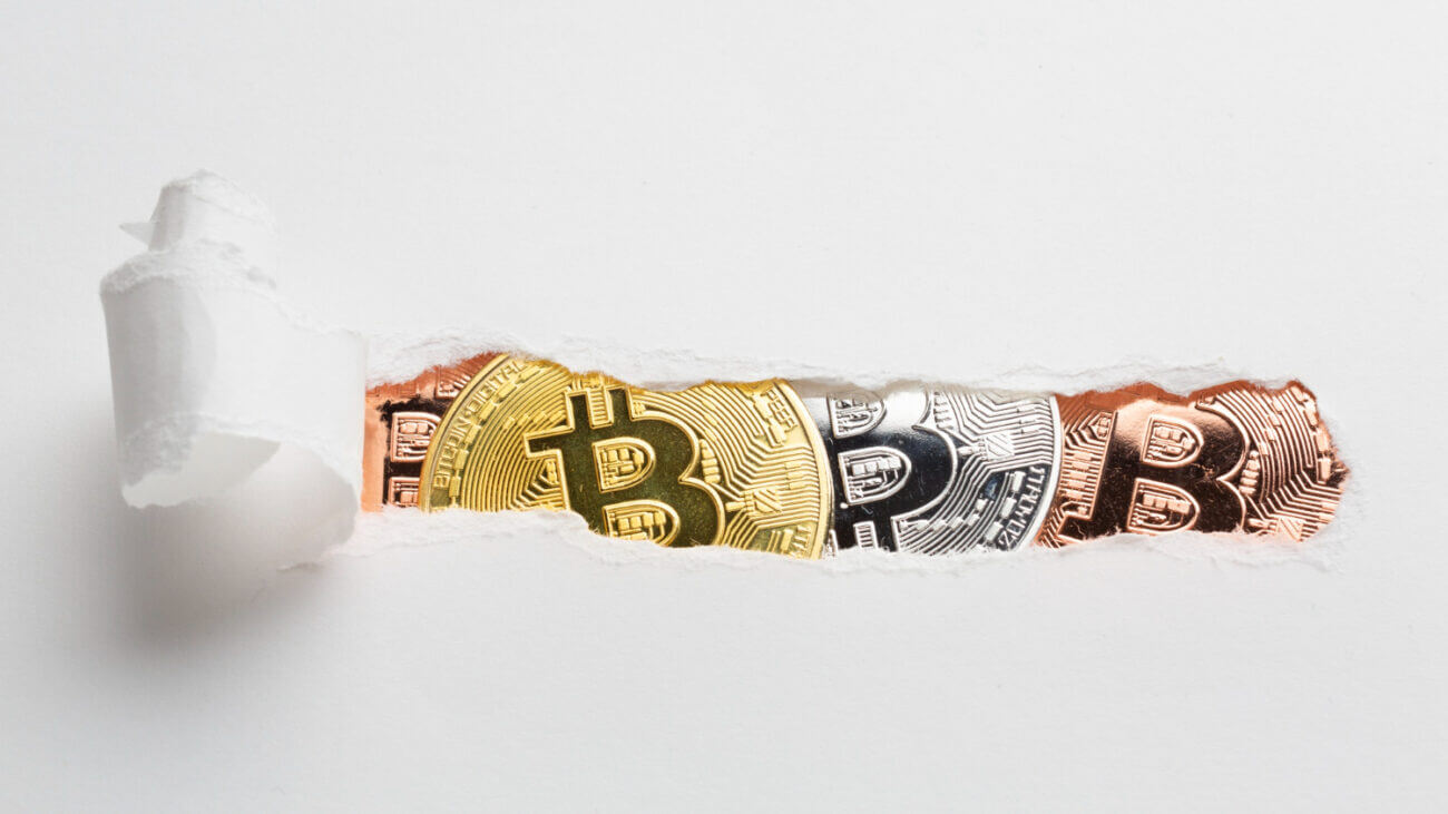 A strip of paper torn open to reveal three coins with Bitcoin logos