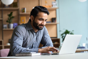 Man smiles while using a laptop at his desk