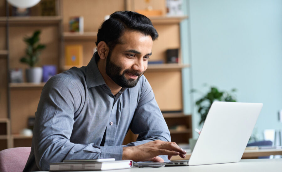 Man smiles while using a laptop at his desk