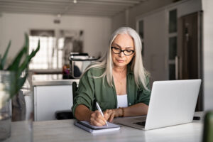 Woman sits at her laptop and makes notes in a notebook