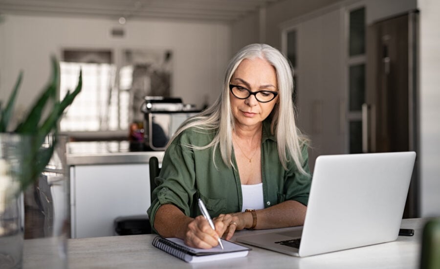 Woman sits at her laptop and makes notes in a notebook