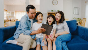 Parents and two young kids sit on a sofa and watch a tablet