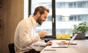 A man drinks from his coffee while reading about U.S. withholding tax rules on his computer