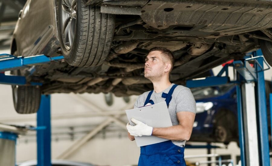 Mechanic with a clipboard stands under a hoisted car