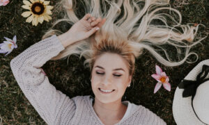 A woman lies in the grass with her eyes closed, smiling