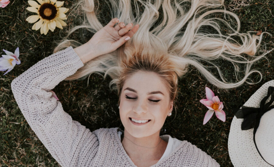 A woman lies in the grass with her eyes closed, smiling