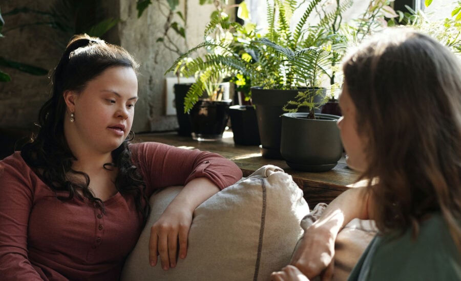 A mother and daughter are seated on a couch discussing plans for a disabled beneficiary trust