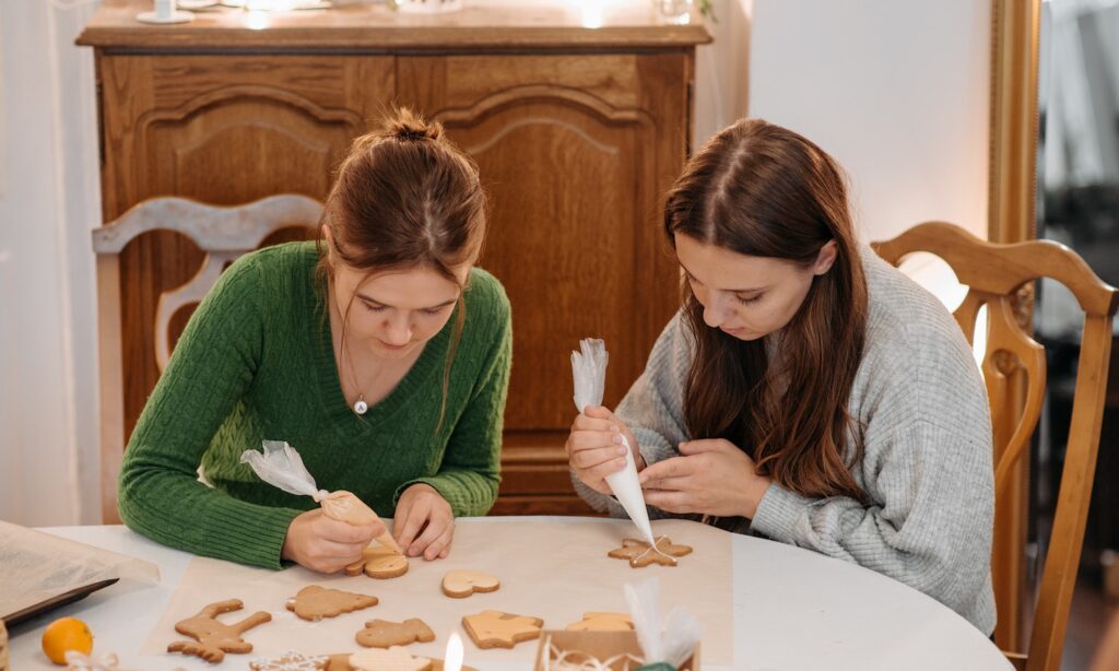 Two teenage girls add icing to gingerbread cookies