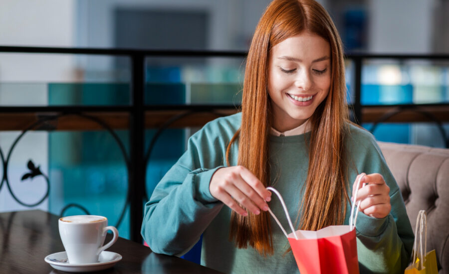 A smiling woman at a cafe looks into a shopping bag