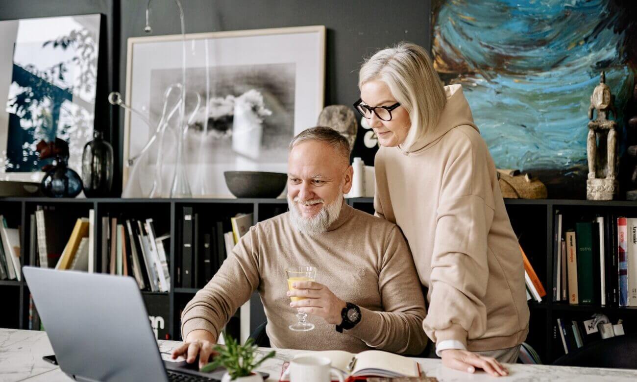 Middle-aged man and woman smile at a laptop as they check their retirement savings